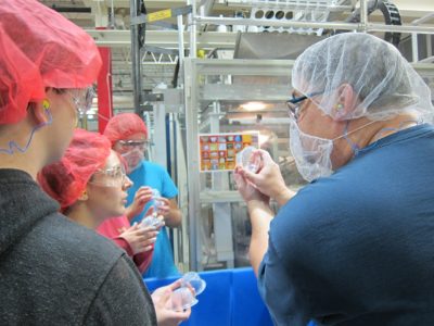 David Rieger, a thermaforming manager at Printpack shows Jamestown students how to find the Printpack logo on cups. (Kirsten Petersen/ WYDaily)