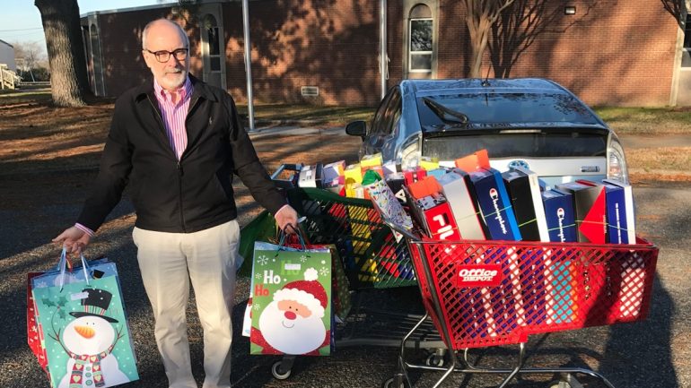 Bill Hoffman holds holiday bags next to a shopping cart filled with shoe donations (WYDaily file/ Courtesy of Bill Hoffman)